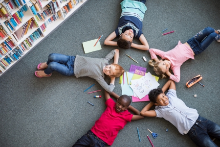 Cinq enfants allongés sur le dos au milieu d'une bibliothèque