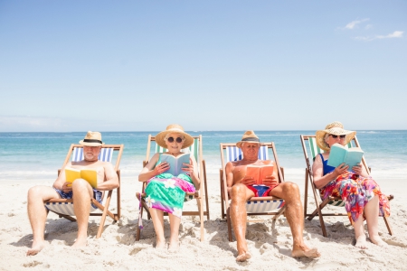 Quatre personnes âgées lisent sur des transats sur la plage