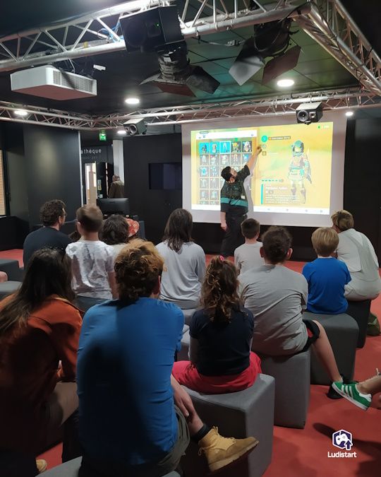 des spectateurs regardent un animateur montrer le jeu sur un écran